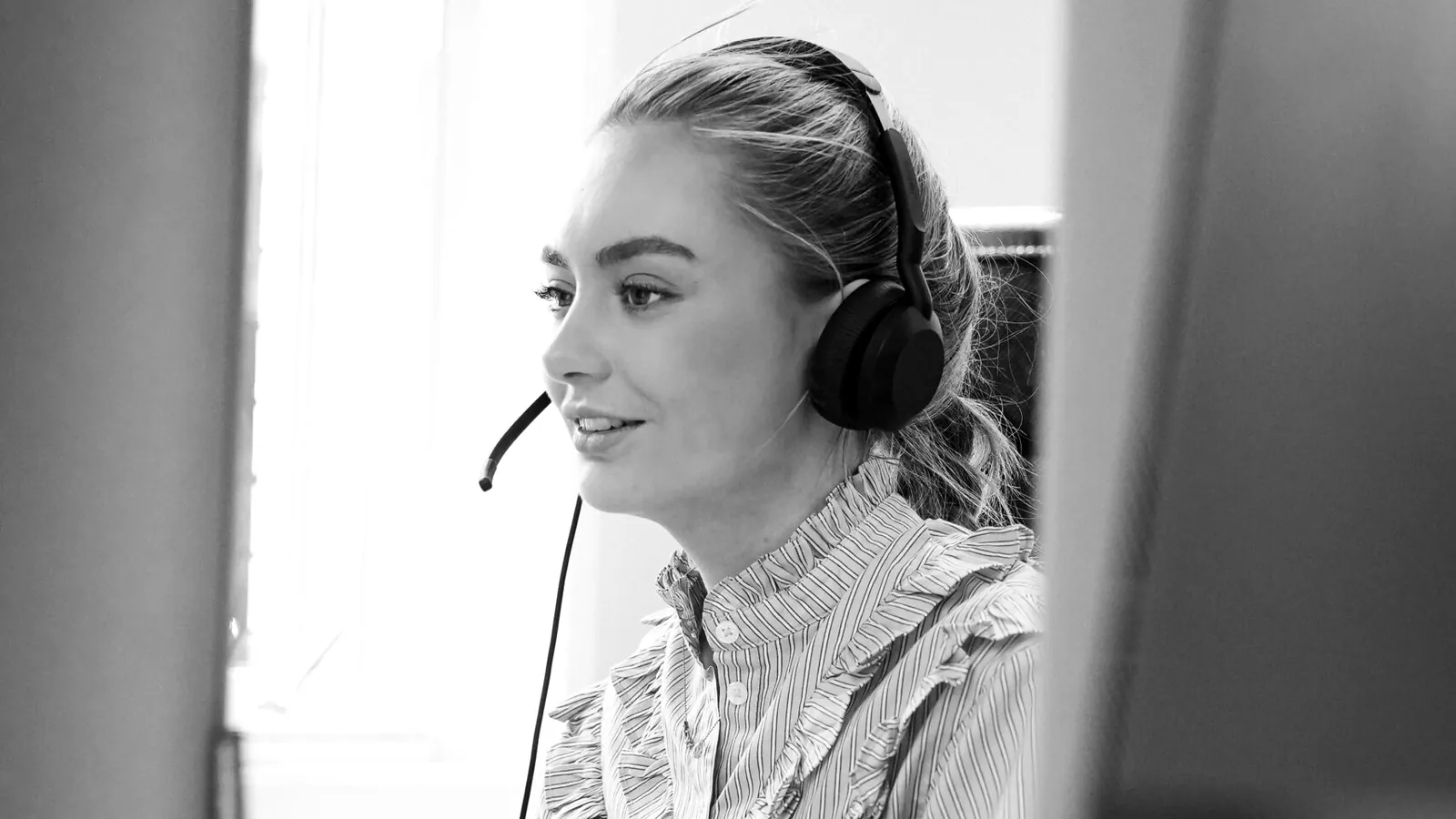 Smilende selger med headset i samtale ved arbeidsplassen