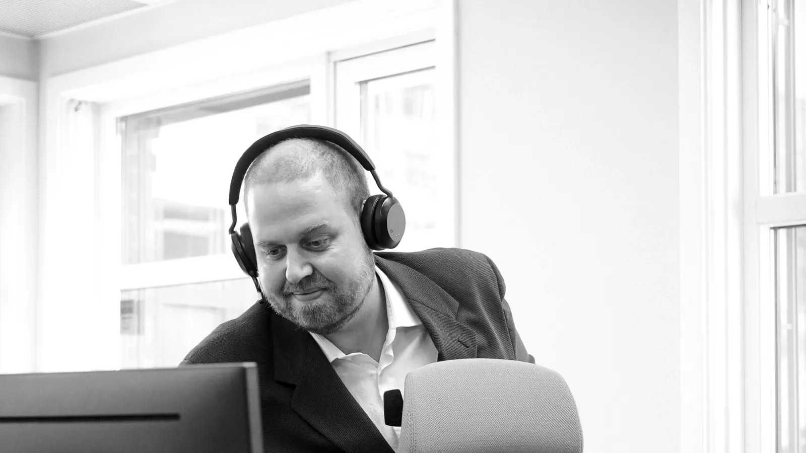 Selger i dressjakke og headset ved arbeidsplassen sin