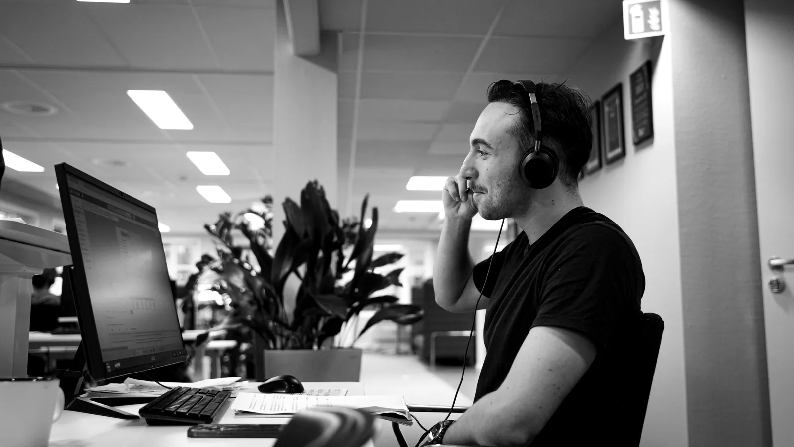 Selger med hodetelefoner i samtale ved skrivebordet sitt